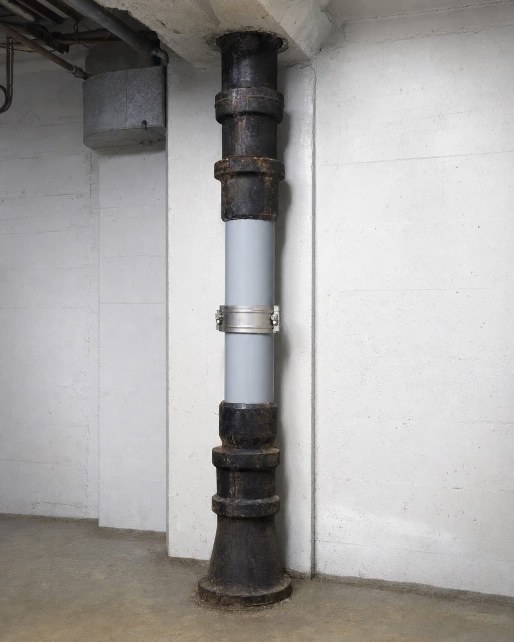 Une colonne de chute en fonte dans un sous-sol d’immeuble, un tronçon remplacé par une canalisation chemisée