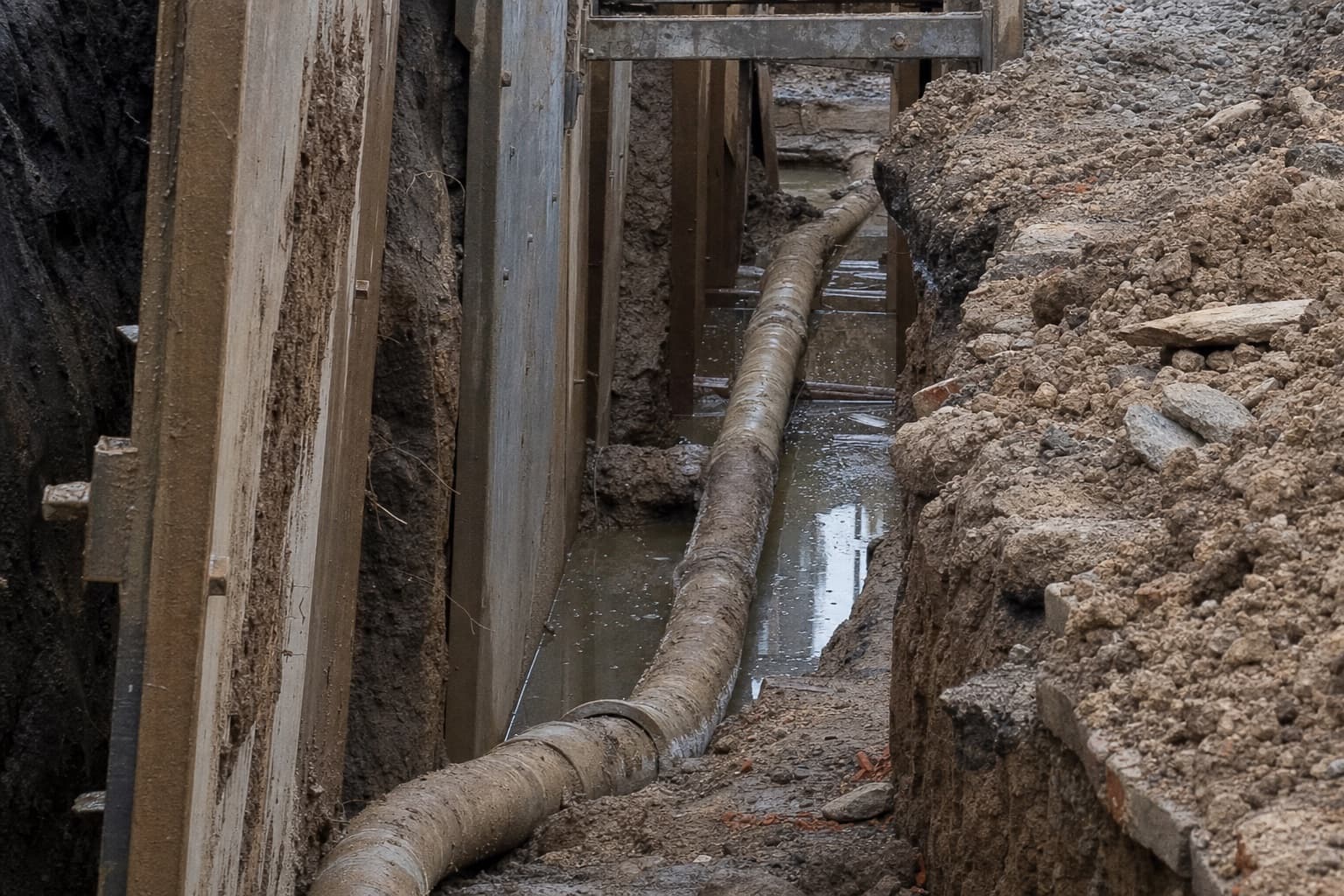 Une section de canalisation dégagée en fouille, un tronçon affaissé retenant de l’eau, la tranchée étayée