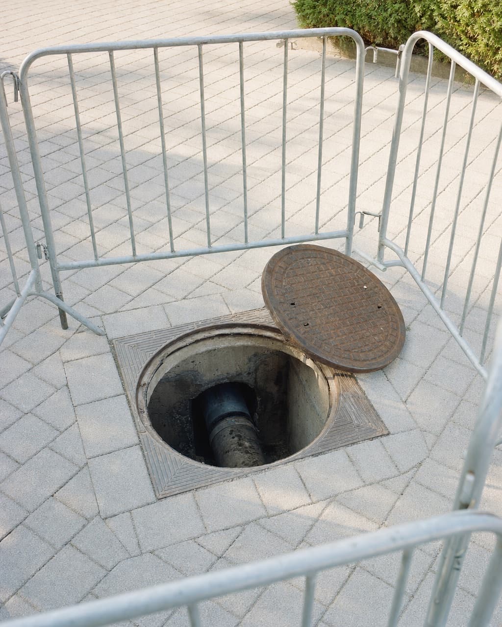 Un regard de visite ouvert dans une cour pavée, la canalisation visible en fond de regard